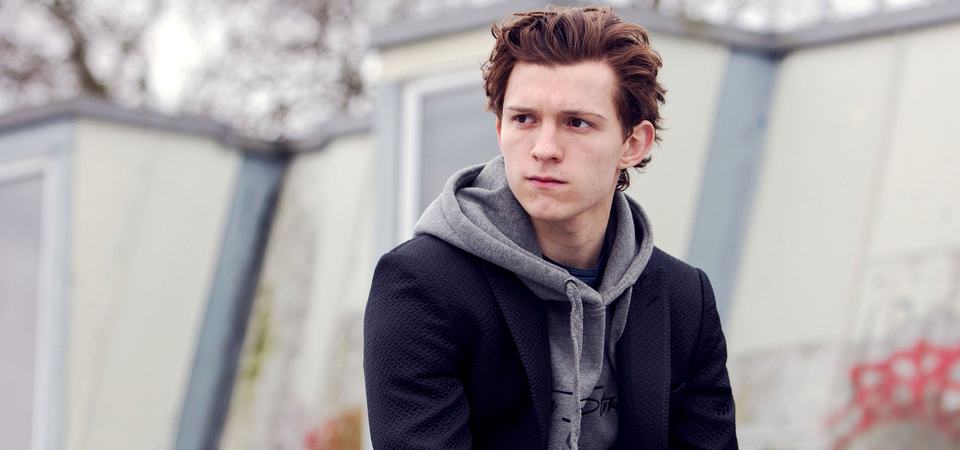 Tom Holland as Peter Parker sitting alone outdoors in a hoodie and coat, looking off to one side