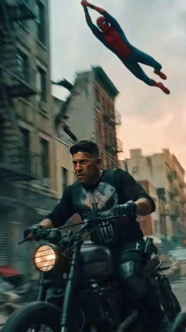 Spider-Man swinging low over the Punisher riding a motorcycle through a city street