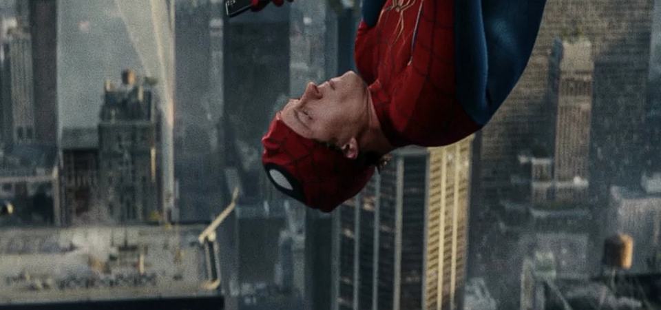 Spider-Man hanging upside down against a moody, overcast New York skyline